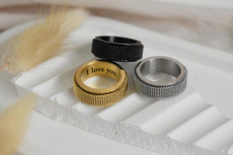Three rings are displayed on a white surface, with one ring featuring a message engraved on it.