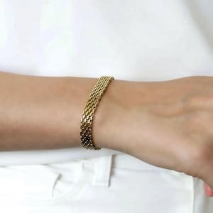 A gold bracelet is worn on a person's wrist.