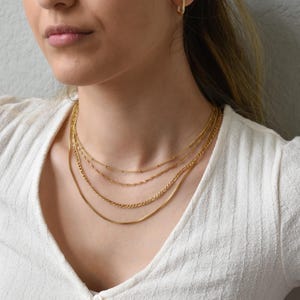 A close-up of a woman wearing a white sweater and multiple gold necklaces.