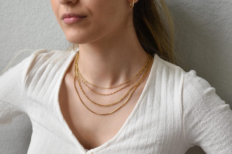 A close-up of a woman wearing a white sweater and multiple gold necklaces.