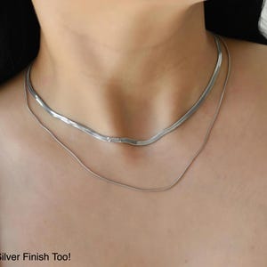 A close-up view of a woman's neck and chest area, showing a silver necklace with a long chain.