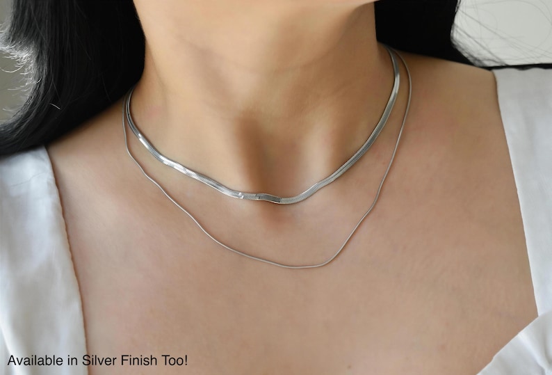 A close-up view of a woman's neck and chest area, showing a silver necklace with a long chain.