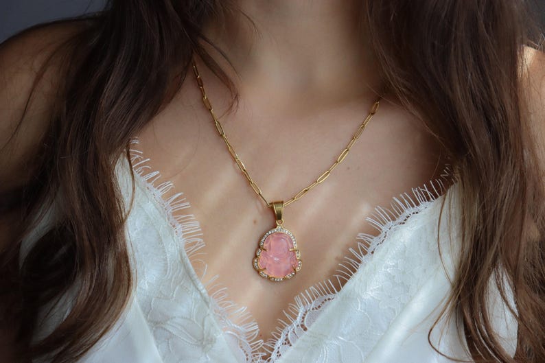 A close-up of a woman's neck and chest wearing a gold necklace with a pink gemstone pendant.