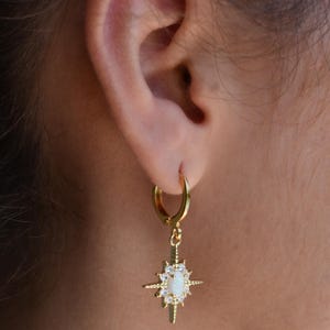 A close-up view of a person's ear wearing a gold hoop earring with a star-shaped gemstone.