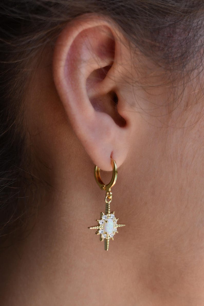 A close-up view of a person's ear wearing a gold hoop earring with a star-shaped gemstone.