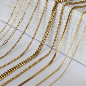 a collection of various gold chain necklaces arranged on a white surface.