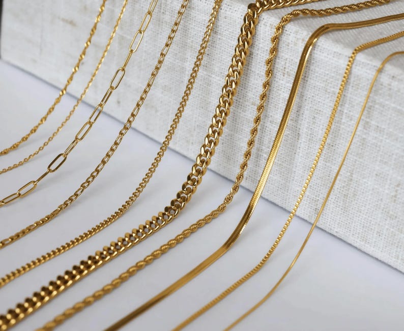 a collection of various gold chain necklaces arranged on a white surface.
