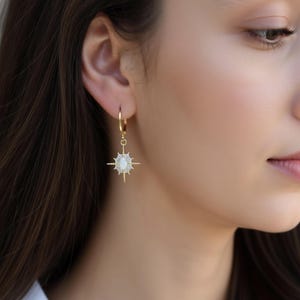 A close-up of a woman's face wearing a pair of gold earrings with a star-shaped gemstone.