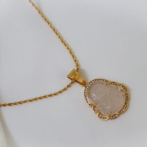 A gold necklace with a pendant featuring a carved stone or gemstone.