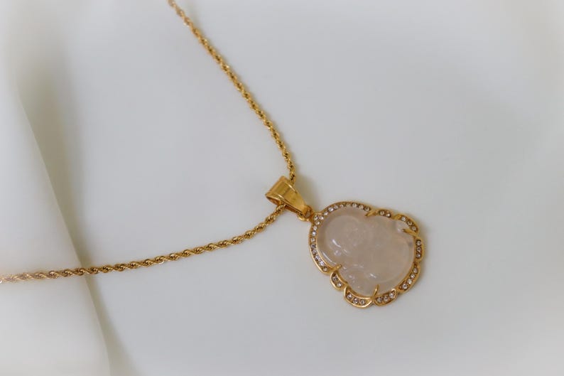 A gold necklace with a pendant featuring a carved stone or gemstone.