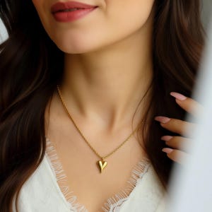 A close-up of a woman's face wearing a gold necklace with a heart-shaped pendant.