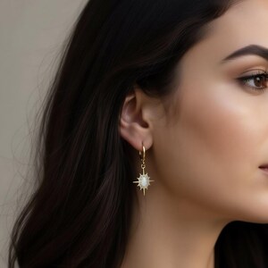 A close-up of a woman's face, focusing on her ear and side profile. She is wearing a pair of gold earrings with a star-shaped pendant.