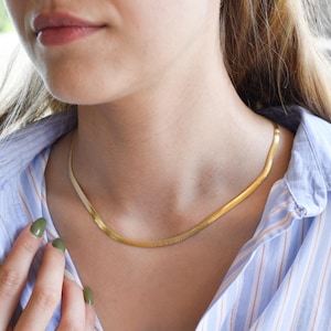 A close-up of a woman wearing a gold necklace and a striped blue and white shirt, with her hand partially visible.