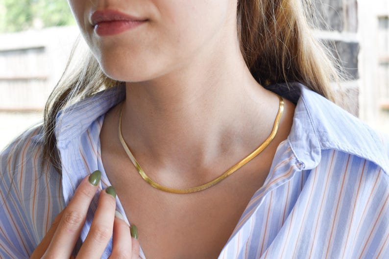 A close-up of a woman wearing a gold necklace and a striped blue and white shirt, with her hand partially visible.
