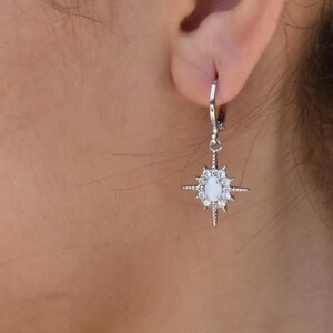 A close-up view of a person's ear adorned with a pair of silver earrings featuring a star-shaped charm.