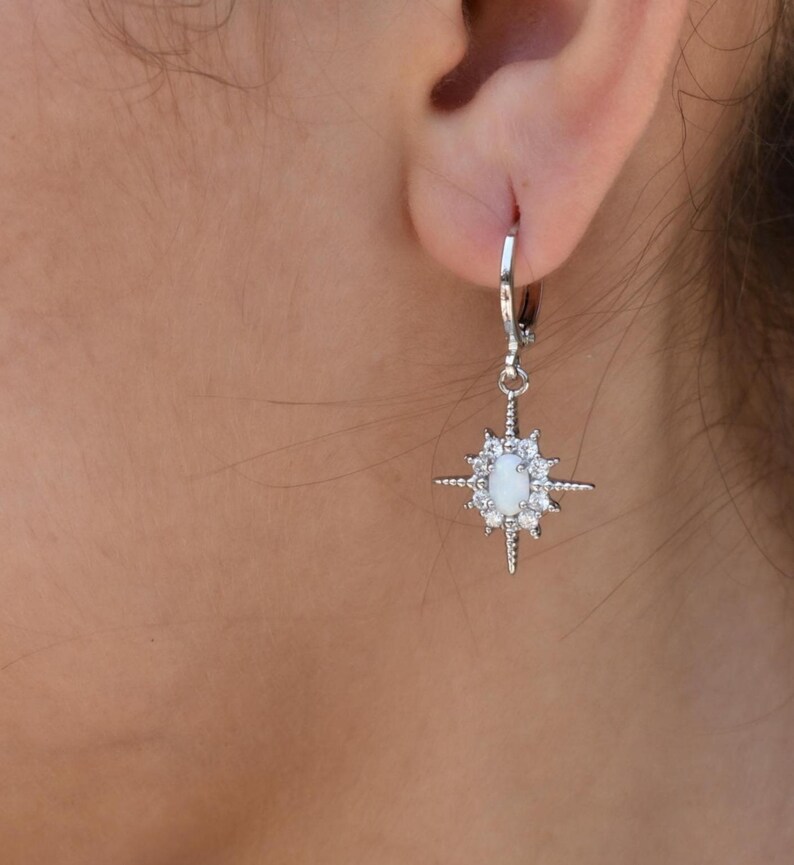 A close-up view of a person's ear adorned with a pair of silver earrings featuring a star-shaped charm.