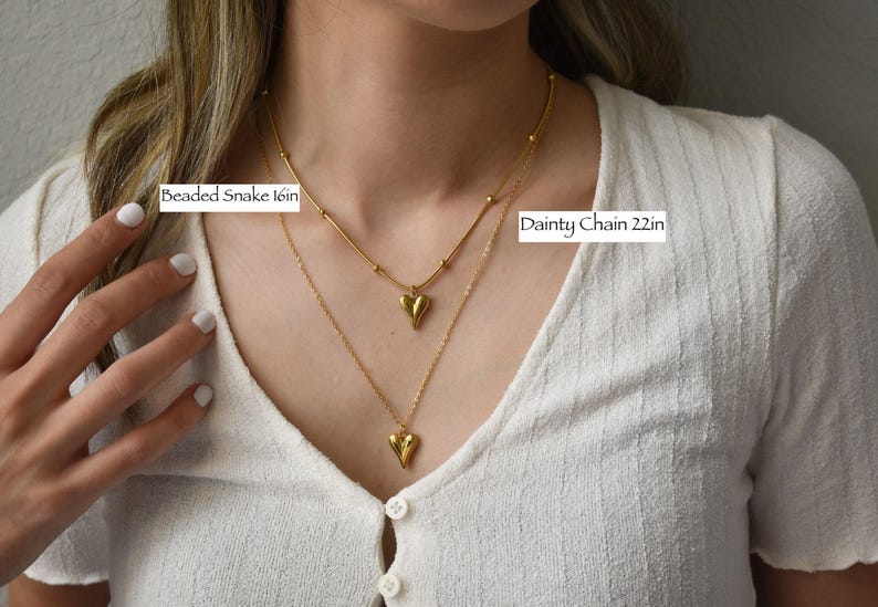 A close-up of a person's neck and chest wearing two gold necklaces, with labels indicating the size of the necklace.