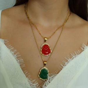 A woman wearing a white lace top and two gold necklaces with Buddha pendants.