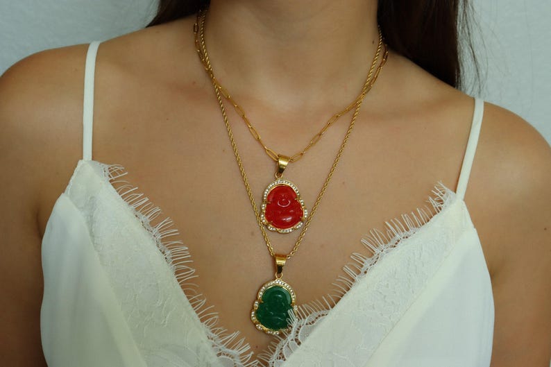 A woman wearing a white lace top and two gold necklaces with Buddha pendants.