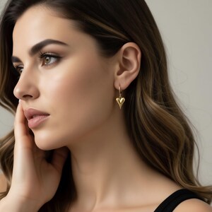 A close-up portrait of a woman with long, wavy brown hair wearing a gold heart-shaped earring.