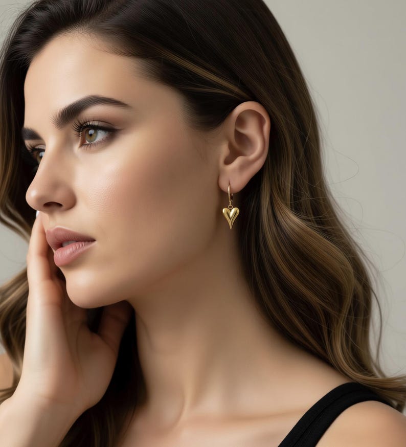 A close-up portrait of a woman with long, wavy brown hair wearing a gold heart-shaped earring.