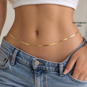 A close-up of a person wearing a white crop top and blue jeans, with a gold-colored belt around the waist.
