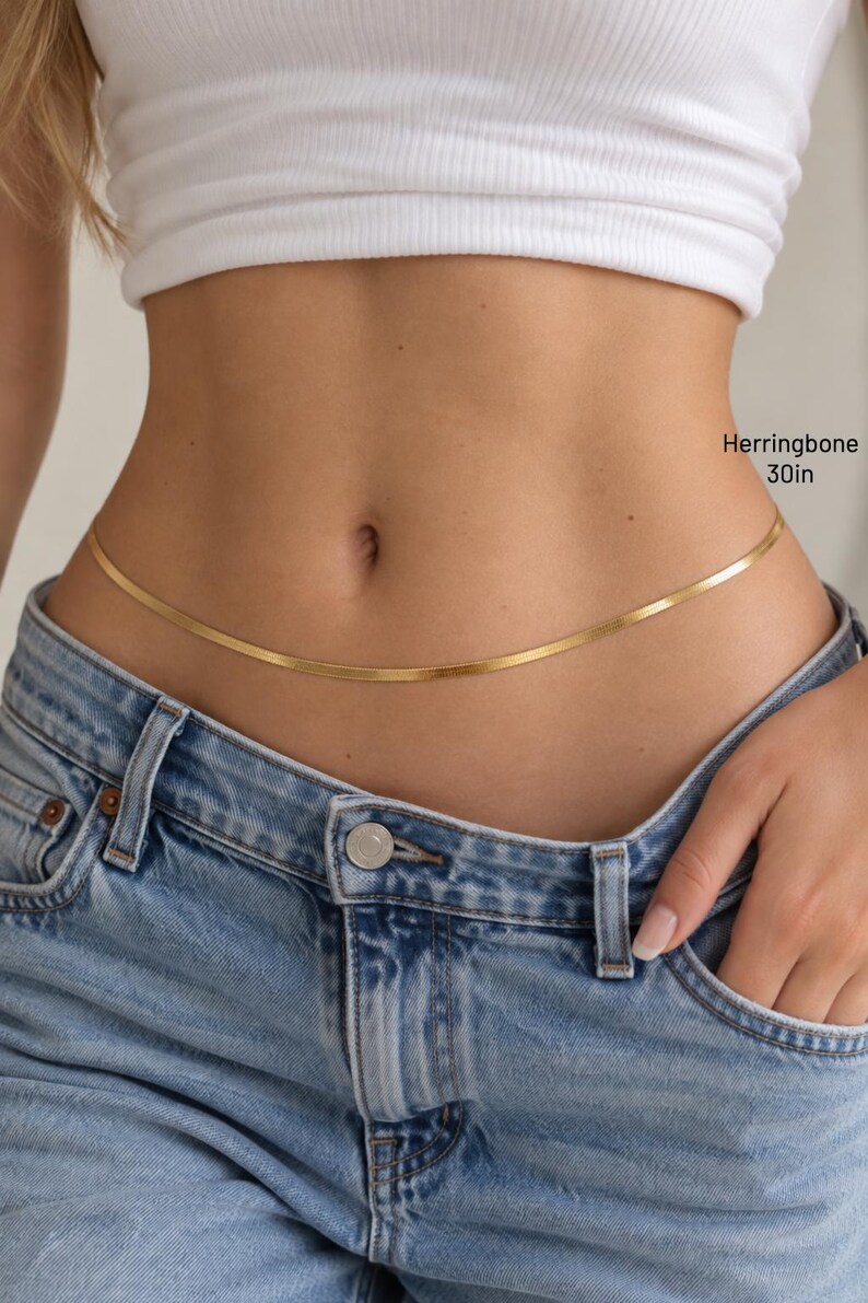 A close-up of a person wearing a white crop top and blue jeans, with a gold-colored belt around the waist.