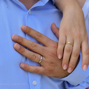 A close-up image of a couple's hands, with the man's hand wearing a wedding ring and the woman's hand wearing a gold ring.
