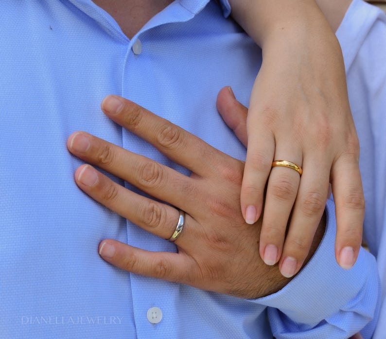 A close-up image of a couple's hands, with the man's hand wearing a wedding ring and the woman's hand wearing a gold ring.