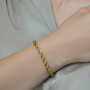 A close-up of a person's hand wearing a gold bracelet and necklace, with their hair visible.