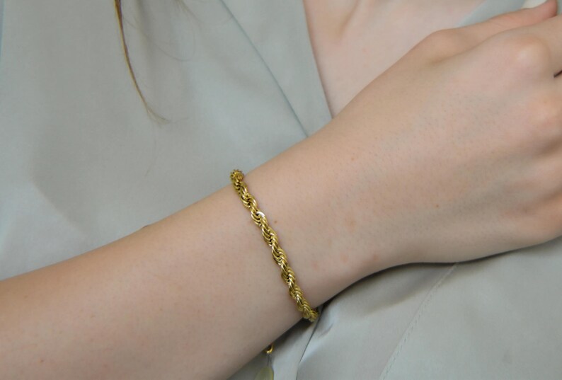 A close-up of a person's hand wearing a gold bracelet and necklace, with their hair visible.