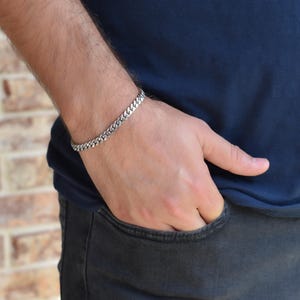 A close-up view of a person's hand wearing a silver bracelet, with their hand in a pocket.