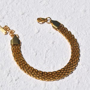A gold-colored bracelet with a chain-like design is shown against a white background.