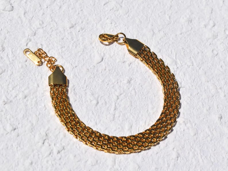 A gold-colored bracelet with a chain-like design is shown against a white background.