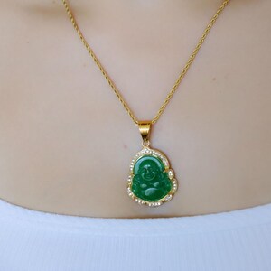 A woman wearing a gold necklace with a green Buddha pendant and a gold chain necklace.