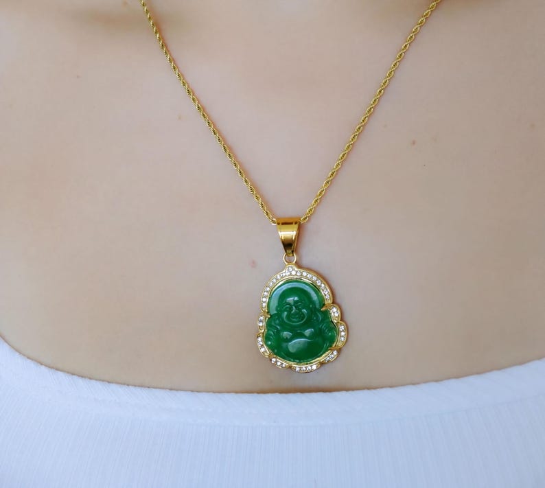 A woman wearing a gold necklace with a green Buddha pendant and a gold chain necklace.