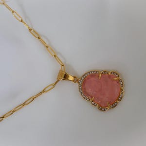 a gold necklace with a heart-shaped pendant and a red gemstone.