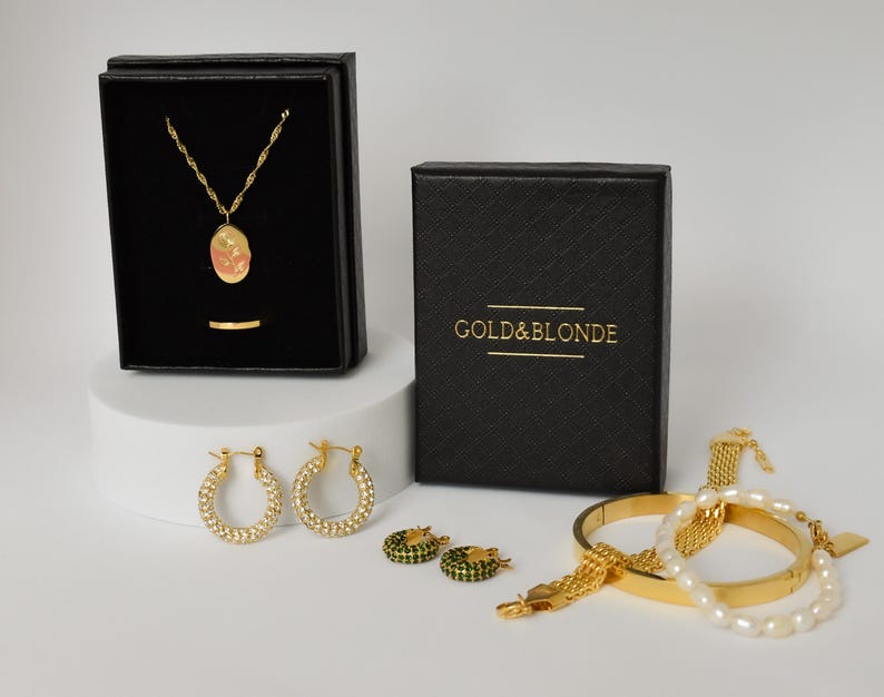 a collection of gold and silver jewelry and accessories, including a necklace, earrings, a bracelet, and a box, all presented in a black and gold color scheme.
