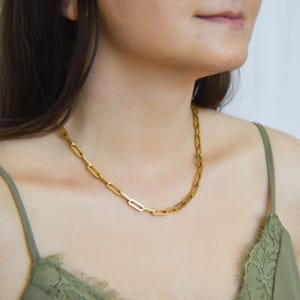 A close-up of a woman wearing a gold chain necklace with a green lace bra strap.
