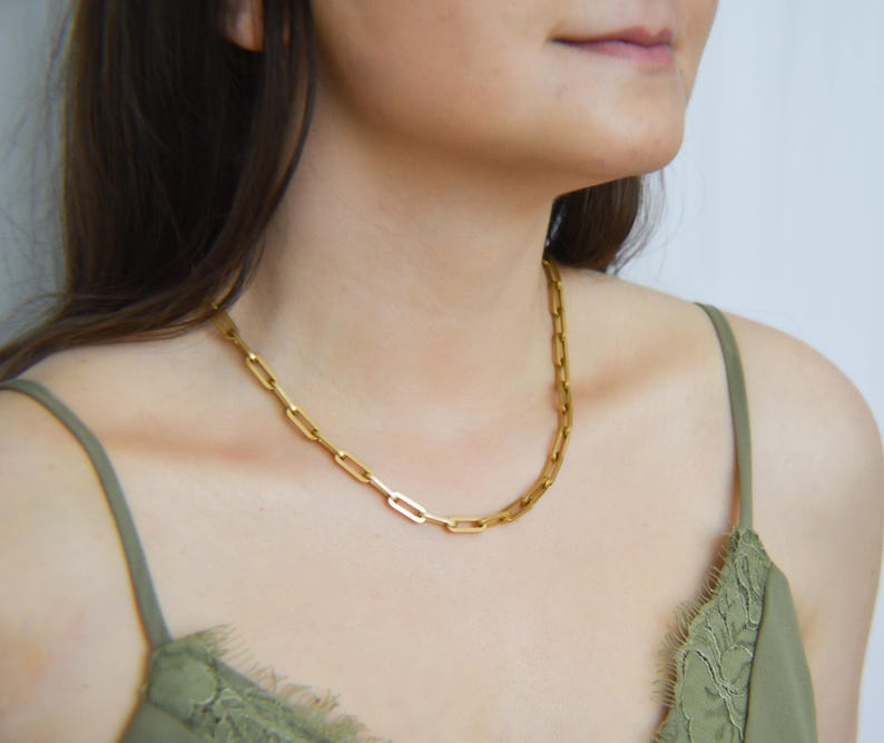 A close-up of a woman wearing a gold chain necklace with a green lace bra strap.