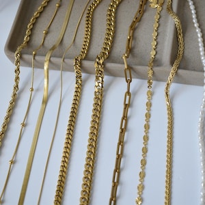 a variety of gold necklaces and chains arranged on a white surface.