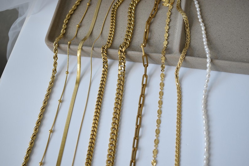 a variety of gold necklaces and chains arranged on a white surface.