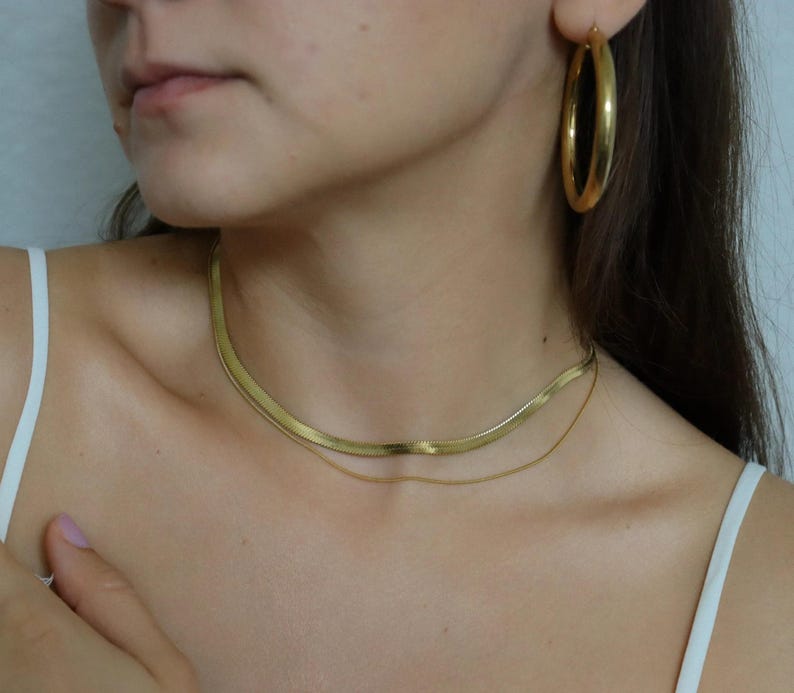 A close-up of a woman's neck and chest area, featuring a gold necklace and hoop earrings.