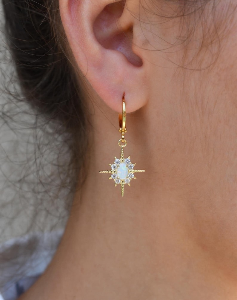 A close-up view of a person's ear wearing a pair of gold earrings with a star-shaped gemstone.