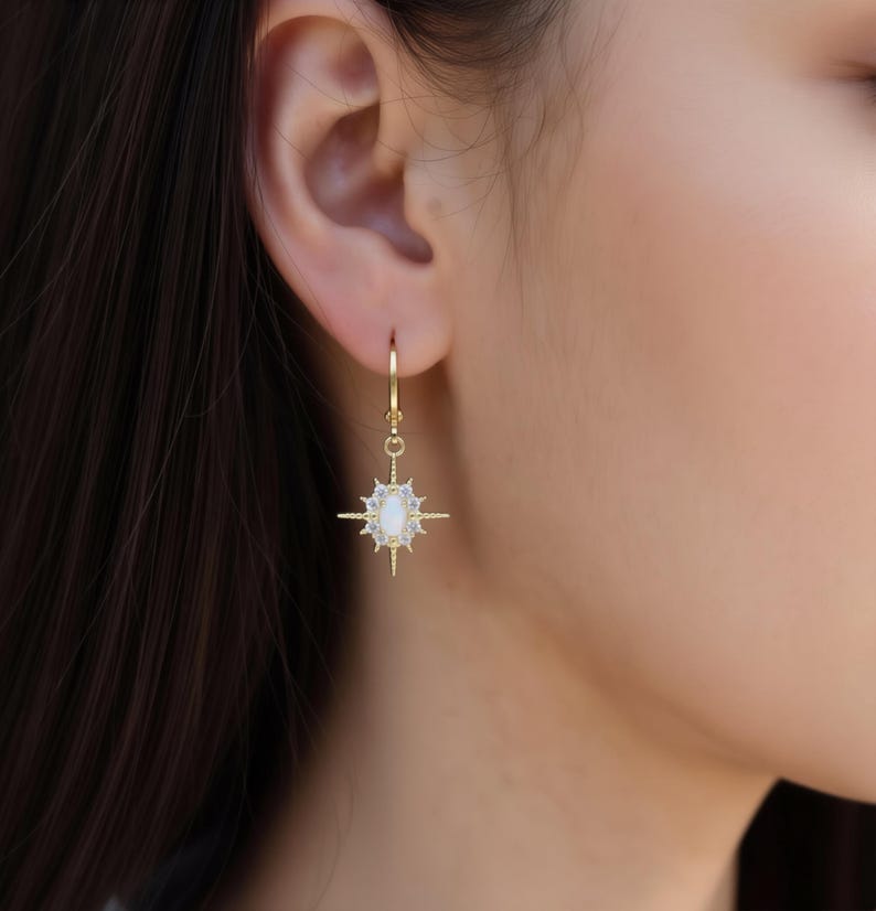 A close-up view of a person's ear wearing a pair of gold earrings with a star-shaped charm.