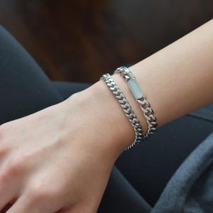 A close-up view of a person's wrist wearing two silver metal bracelets.