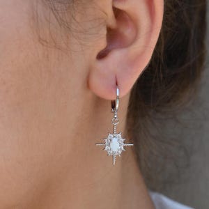 A close-up view of a person's ear wearing a pair of silver earrings with a star-shaped gemstone.