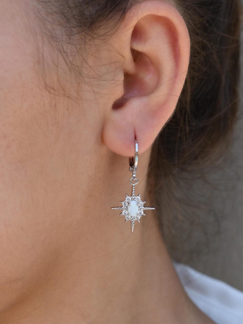 A close-up view of a person's ear wearing a pair of silver earrings with a star-shaped gemstone.