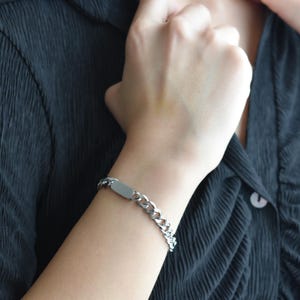 A close-up view of a person's hand wearing a silver bracelet, with a dark-colored shirt underneath.