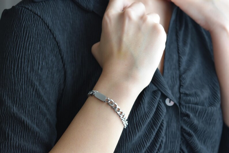 A close-up view of a person's hand wearing a silver bracelet, with a dark-colored shirt underneath.